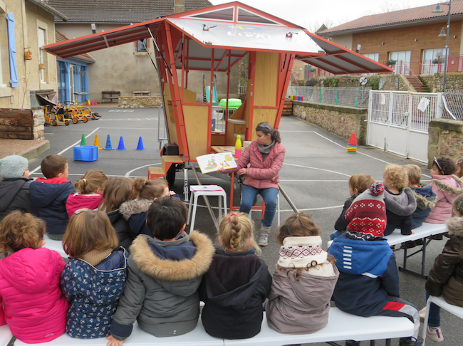 Une bibliothécaire lit un album devant une classe de jeunes enfants.